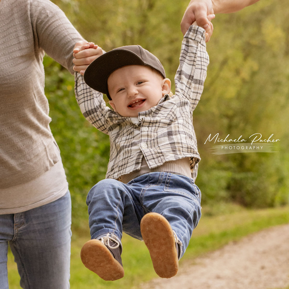 Kleiner Junge lacht ausgelassen, während er von zwei Erwachsenen an den Händen gehalten und spielerisch in die Luft geschwungen wird.